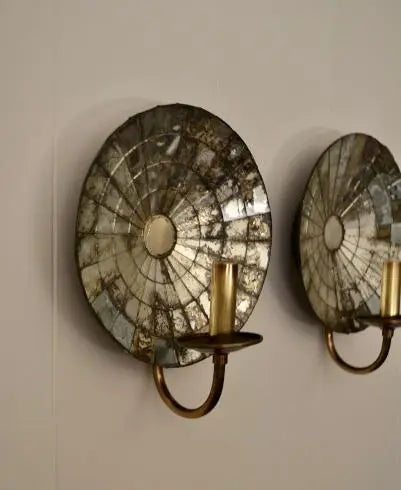 Angled view of two mirrored glass wall sconces with concentric segments and brass candle supports.