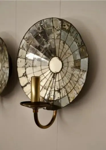Close-up of a single antique mirrored wall sconce with round reflective backing and curved brass candle holder.