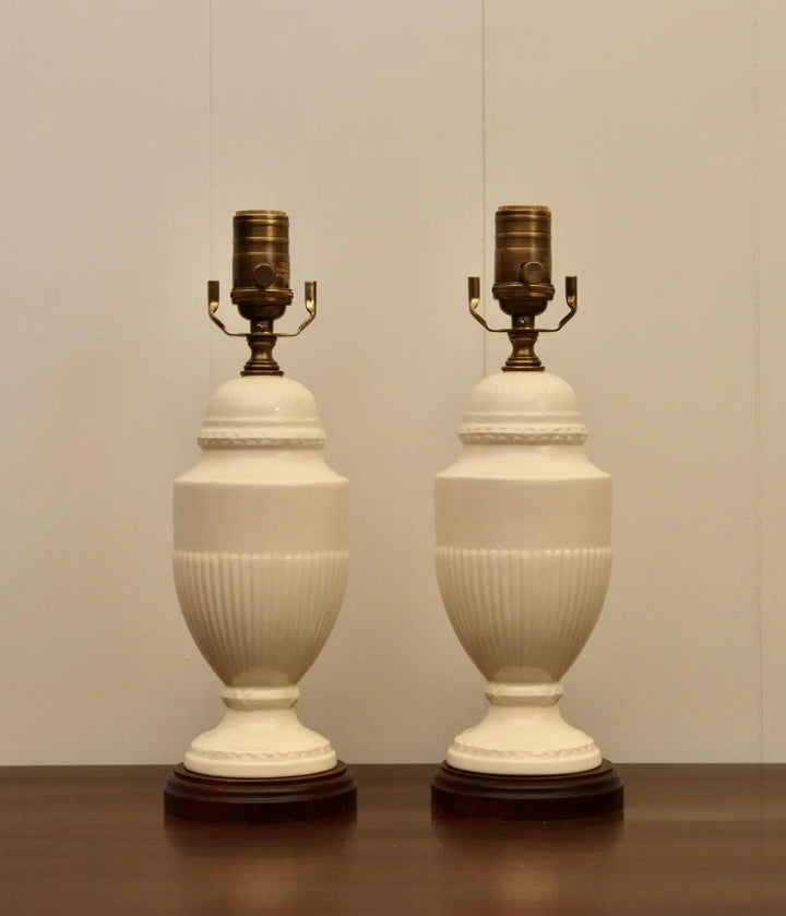 Pair of classic vintage cream ceramic table lamps with brass fittings and decorative bases on a wooden table.