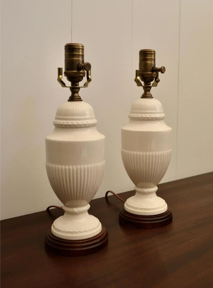 Angled view of two vintage cream ceramic lamps with brass hardware resting on wooden bases.