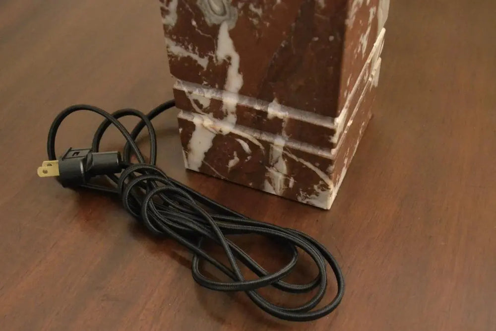 Close-up of electrical cord and base of red marble table lamp with white veining