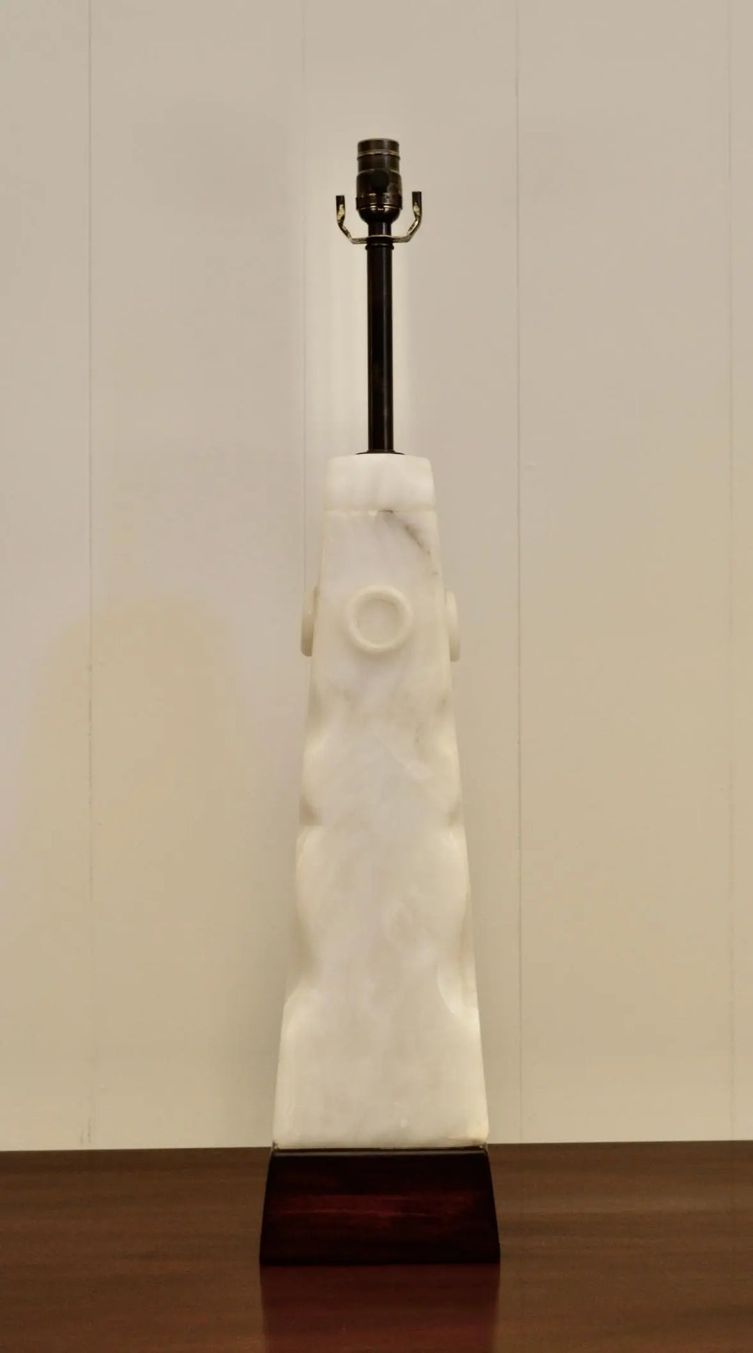 Front view of sculptural white alabaster lamp with circular carvings and wood base.