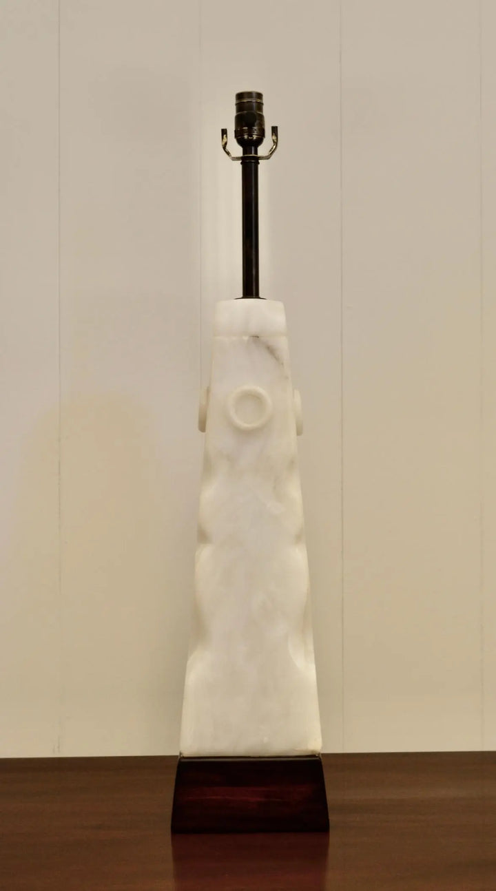 Front view of sculptural white alabaster lamp with circular carvings and wood base.