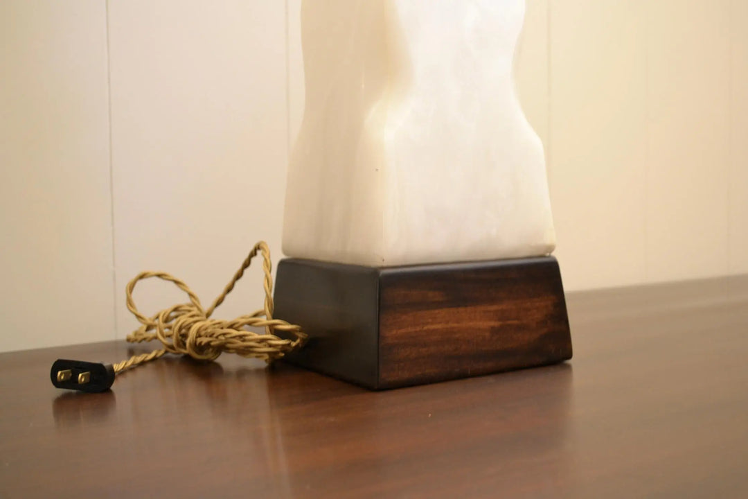 Detail of twisted fabric cord exiting from dark wood base of alabaster lamp.
