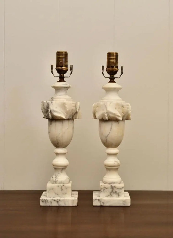 Front view of two classical white marble table lamps with urn-shaped bodies and ornate carved tops