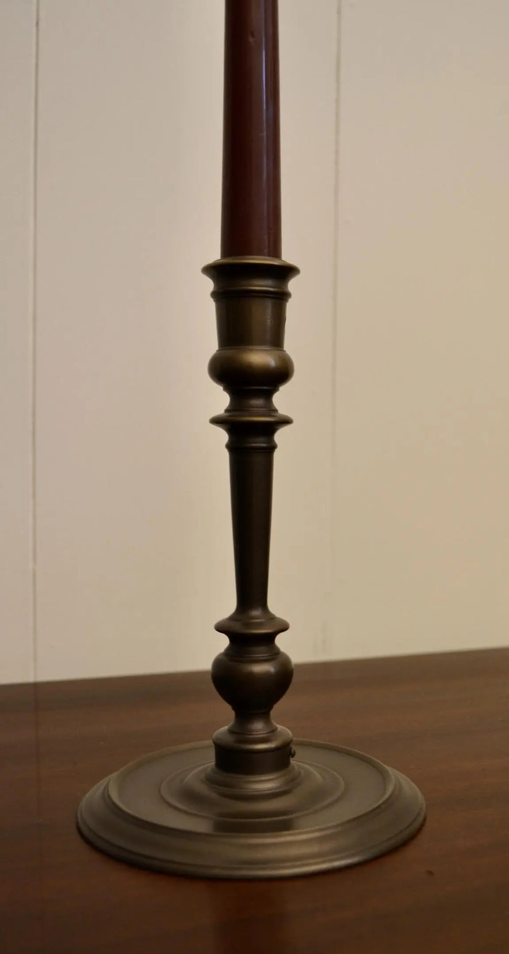 Close-up of antique bronze candlestick holder with rich patina and tall burgundy candle
