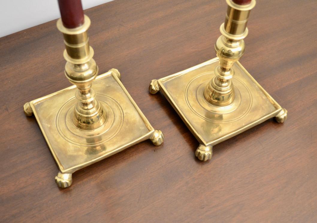 Close-up of brass candlestick holders with engraved concentric circles and claw feet.