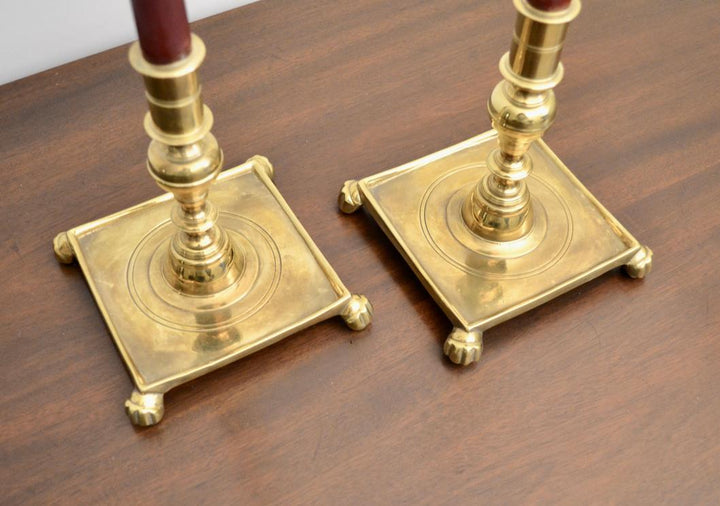 Close-up of brass candlestick holders with engraved concentric circles and claw feet.