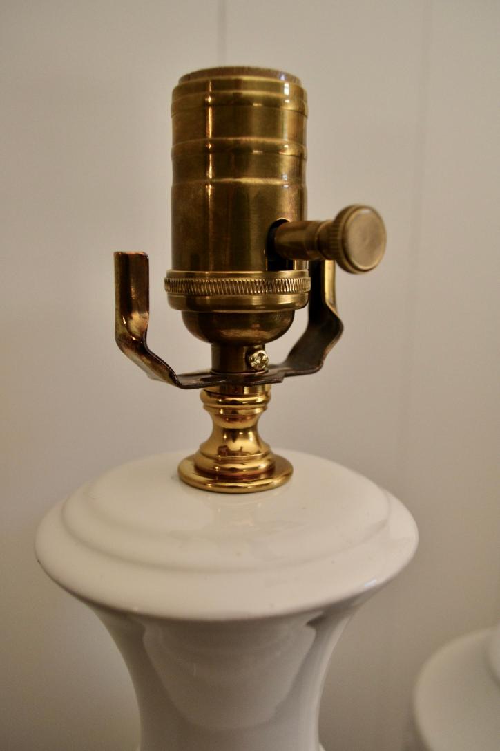 Close-up of brass socket on vintage white ceramic table lamp with harp support brackets