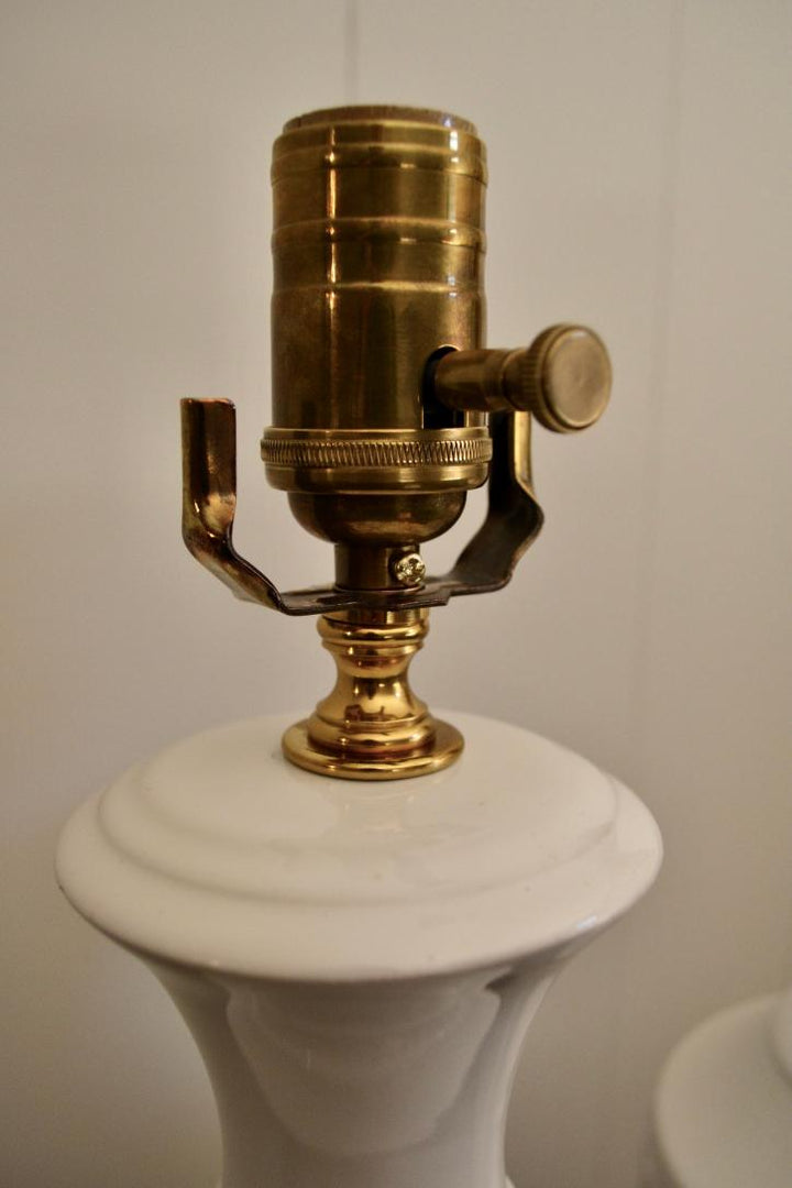 Close-up of brass socket on vintage white ceramic table lamp with harp support brackets